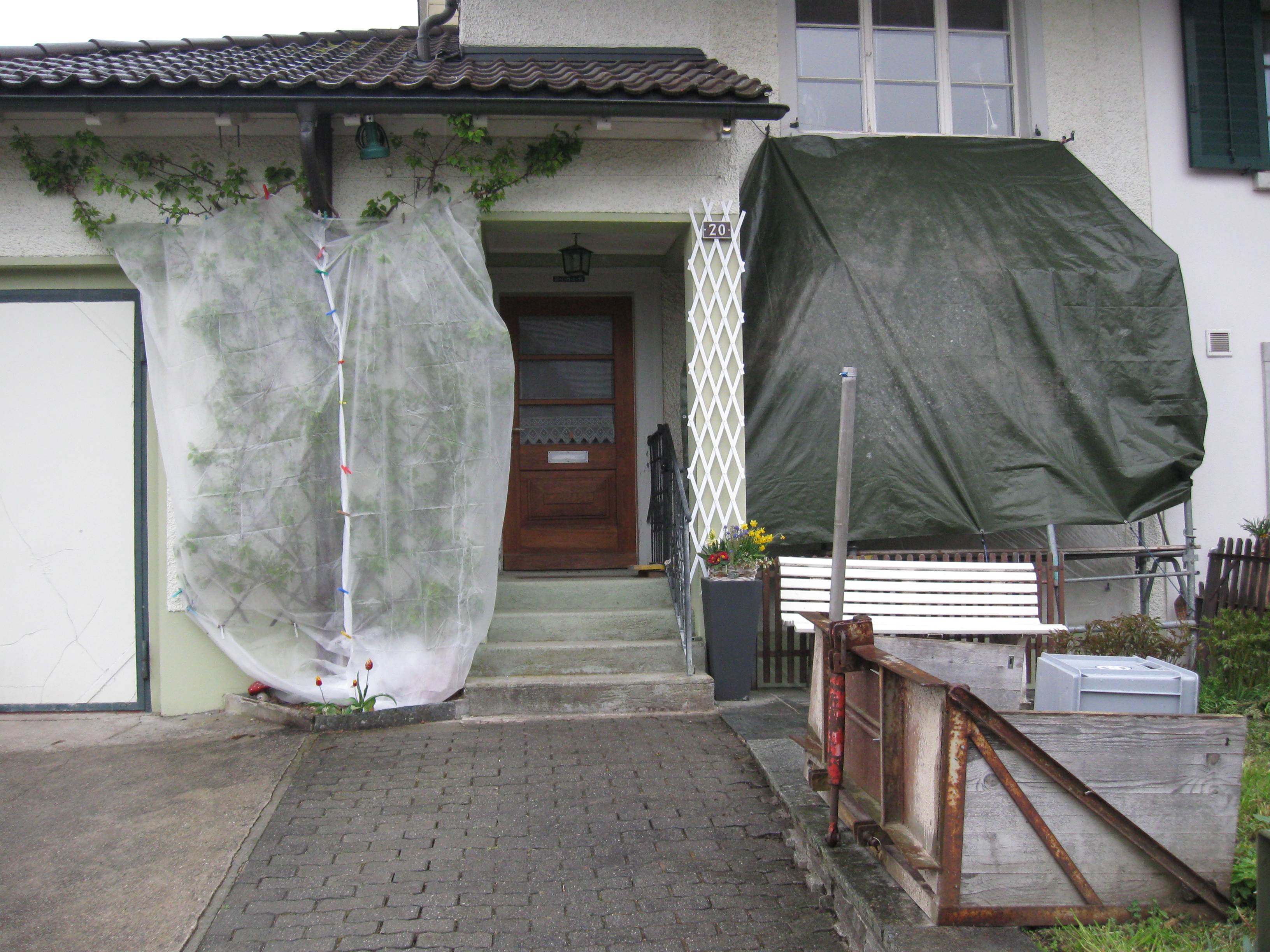 Vor dem Haus wir noch an den Fensterbrüstungen geschliffen und gemalt (hinter grüner Plane)